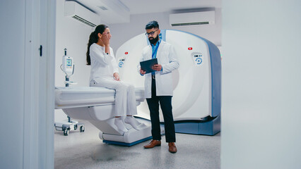 Stressed female touching temples while sitting on diagnostic bed. Bearded male doctor wearing...