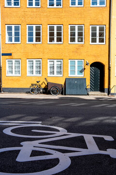 Bike lane sign painted on dark road asphalt in Copenhagen with yellow building in the background creating an urban scene