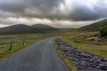 Narrow rural road leading to mountains in atmospheric cloud