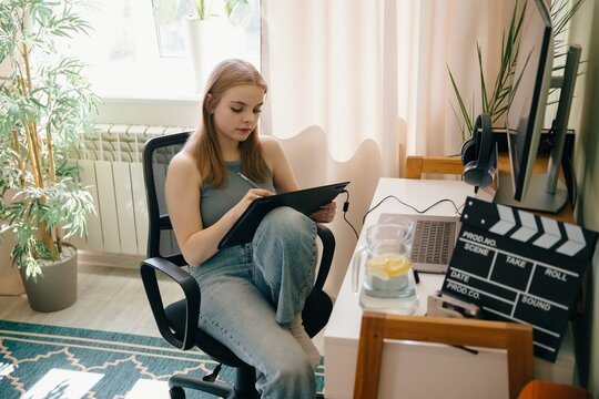 Young woman drawing on tablet at home office desk with movie clapper