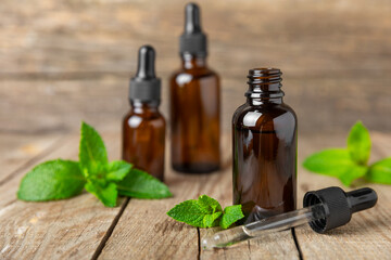 Essential oil mint on a wooden background. Peppermint essential oil with fresh mint leaves. A bottle of aromatherapy oil. Mint extract. The concept of natural cosmetics, spa care. copy space
