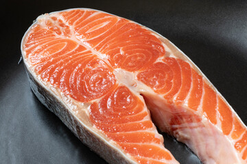 A piece of raw salmon lies in a black plate