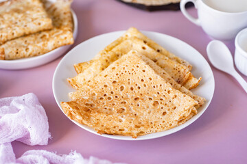 Delicious homemade breakfast: thin large pancakes on a beautiful white plate on a pink background. Thin pancakes for dessert. View from above. Close-up