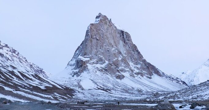 Sacred Gumbo Ronjon mountain in Zanskar Valley, Ladakh, with melting stream and snow-covered winter landscape under cloudy sky