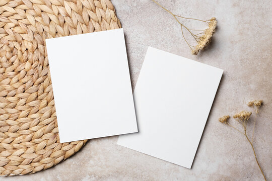 Two blank white vertical wedding invitation cards, front and back sides on beige background with dried flowers and woven placemat. Boho style flat lay with copy space
