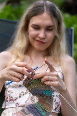 A girl with blond hair crochets a warm scarf
