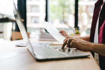 Portrait of a man working with documents using laptop in modern office. Preparing accounting...