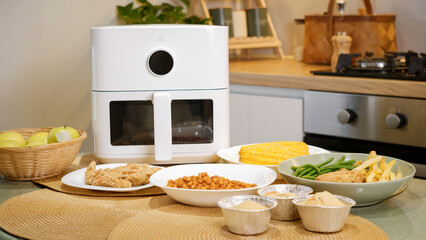 Modern air fryer cooking various dishes in kitchen: chicken, vegetables, and more