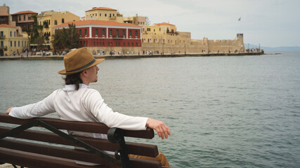 Tourist relaxing on bench enjoying view of chania, crete, greece