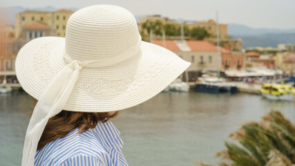 Tourist wearing white sun hat looking at chania venetian harbour in crete, greece