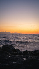 Waves crashing on rocks at sunset with birds flying over the ocean