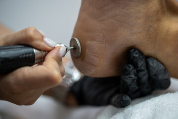 Close-up of professional pedicure using electric callus remover on heel at beauty salon