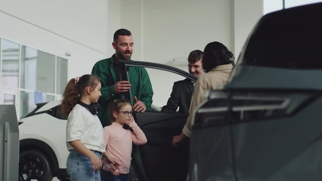 In a modern car dealership, a manager shows and advises a young family with children about buying or test driving a modern car. The concept of buying or leasing a new car.