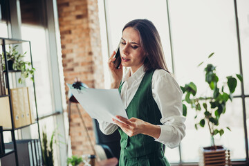 Confident businesswoman analyzing documents while talking on the phone in a modern office environment