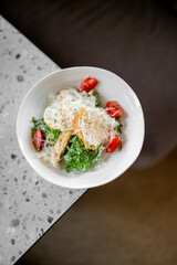 Fresh Caesar salad with croutons, grated cheese, and tomato slices in a white bowl on a speckled...