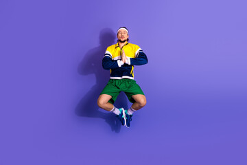 Young athletic man performing a jump in retro activewear against a bright purple background, expressing energy and vitality
