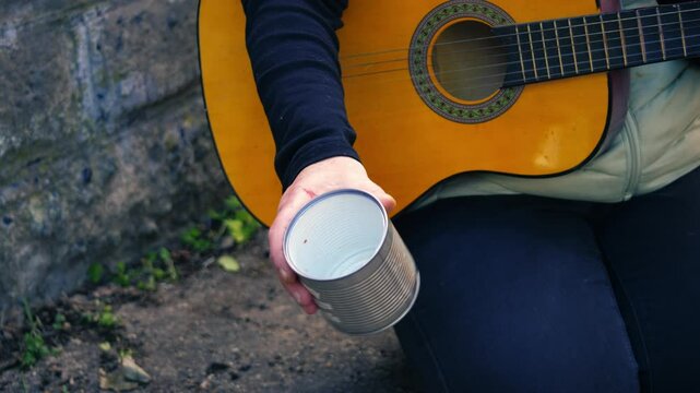 Guitar street busker shaking a tin for money