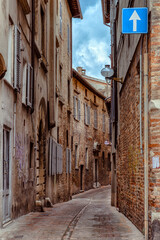 A narrow street in Urbino, a medieval town in Italy, where historic buildings with rustic stone facades tower on either side, creating a serene atmosphere.