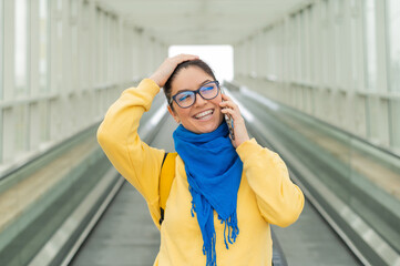 Happy woman stands on a travelator and talks on a cell phone