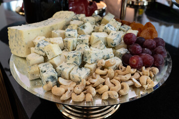 A cheese platter with assorted cheeses, nuts, and grapes displayed on a buffet table in a restaurant. The elegant arrangement offers a gourmet selection perfect for fine dining, wine pairing