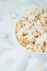 Fresh popcorn in a white bowl on soft fabric background