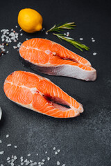 Fresh salmon fillets with lemon and herbs on dark stone background