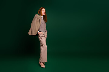 Young businesswoman in a stylish formal outfit posing confidently with an emerald green background...