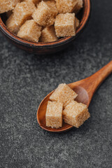 Brown sugar cubes in a wooden bowl and spoon on a dark surface