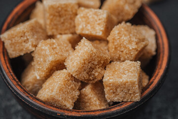 Brown sugar cubes arranged neatly in a rustic bowl on a dark surface