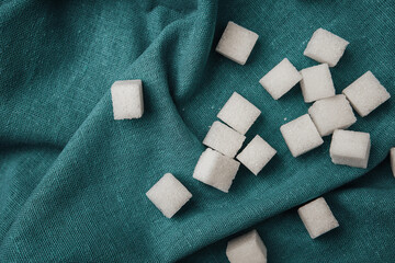 Sugar cubes scattered on a teal fabric background in indoor setting