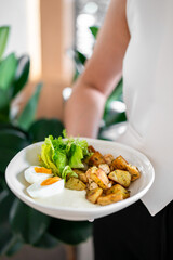 A person holds a plate with a nutritious meal featuring boiled eggs, roasted potatoes, and fresh...