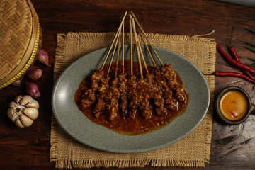 Delicious Indonesian goat satay served on a gray plate with thick peanut sauce. Rustic top view setting.