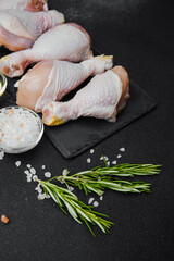 Chicken drumsticks arranged on black slate with herbs and salt