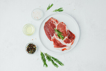 Uncooked pork steak on white plate with rosemary and pepper