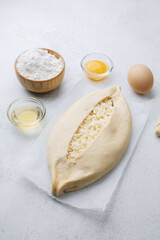 Khachapuri with cheese and baking tools on white kitchen surface