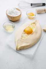 Uncooked khachapuri with egg yolk and whisk on white background