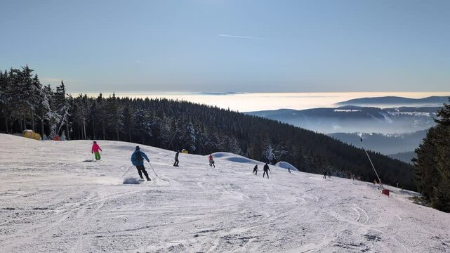 Skiers speed down a snow-covered slope surrounded by woods in winter