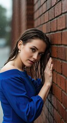 Fototapeta premium Young woman in blue dress leans against a brick wall in the rain. Braided hair and wet appearance create a melancholic atmosphere. The scene focuses on the woman's face with raindrops visible