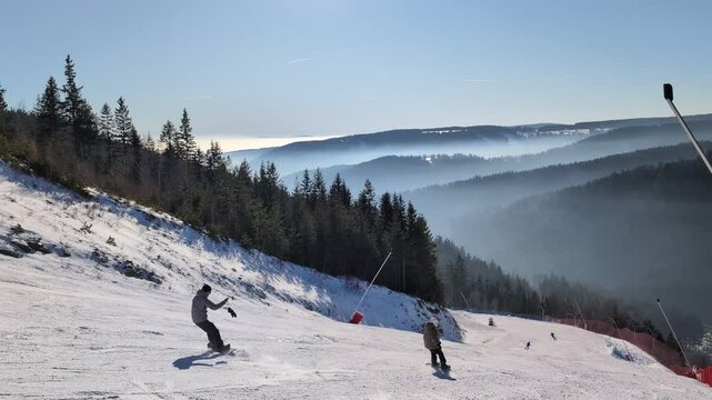 Skiers speed down a snow-covered slope surrounded by woods in winter - view from the hilltop