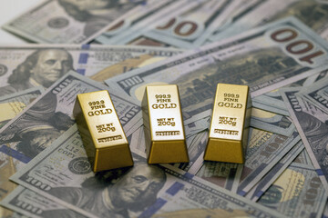 Three gold bars rest on spread of hundred dollar bills, symbolizing wealth and investment. gold...