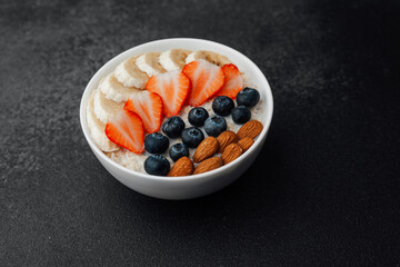 Oatmeal porridge with banana strawberry blueberry and almond toppings on dark background