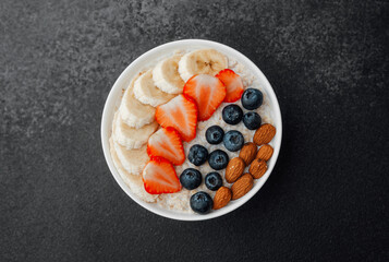 Oatmeal porridge with banana strawberry blueberry and almond toppings on dark background