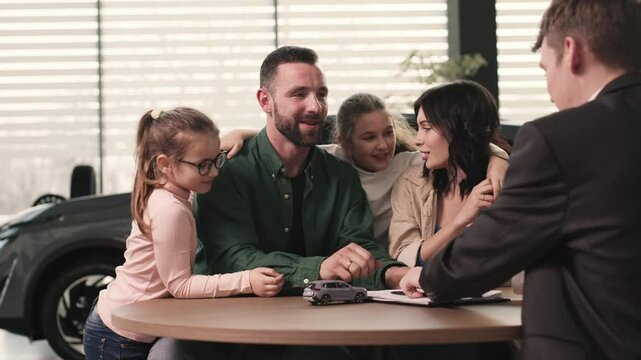 In a modern car dealership, a manager shows and advises a young family with children about buying or test driving a modern car. The concept of buying or leasing a new car.