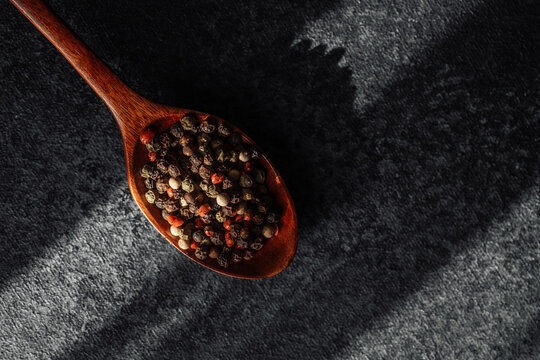 Variety of colorful peppercorns on wooden spoon in sunlight