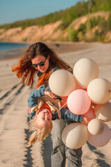A young mother with her daughter little child with balloons by the sea with a beautiful landscape
