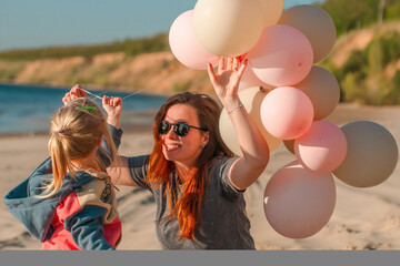 A young mother with her daughter little child with balloons by the sea with a beautiful landscape