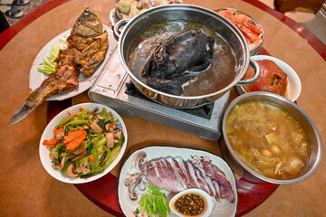  A round dining table set with a traditional Taiwanese home meal centered around black chicken soup, shrimp, vegetables, and various dishes