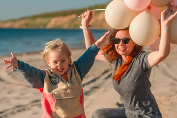 A young mother with her daughter little child with balloons by the sea with a beautiful landscape