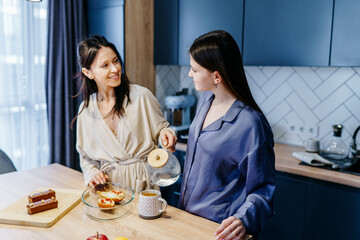 Mother in her 40s and teenage daughter chatting over tea and homemade dessert