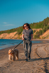 A curly-haired brown Labradoodle or Cavapoo dog with a young woman are best friends by the sea at sunset.